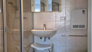 Ein Badezimmer mit Duschkabine aus Glas, einem Waschbecken mit Spiegel darüber, einer Toilette und einem kleinen Trittschemel.