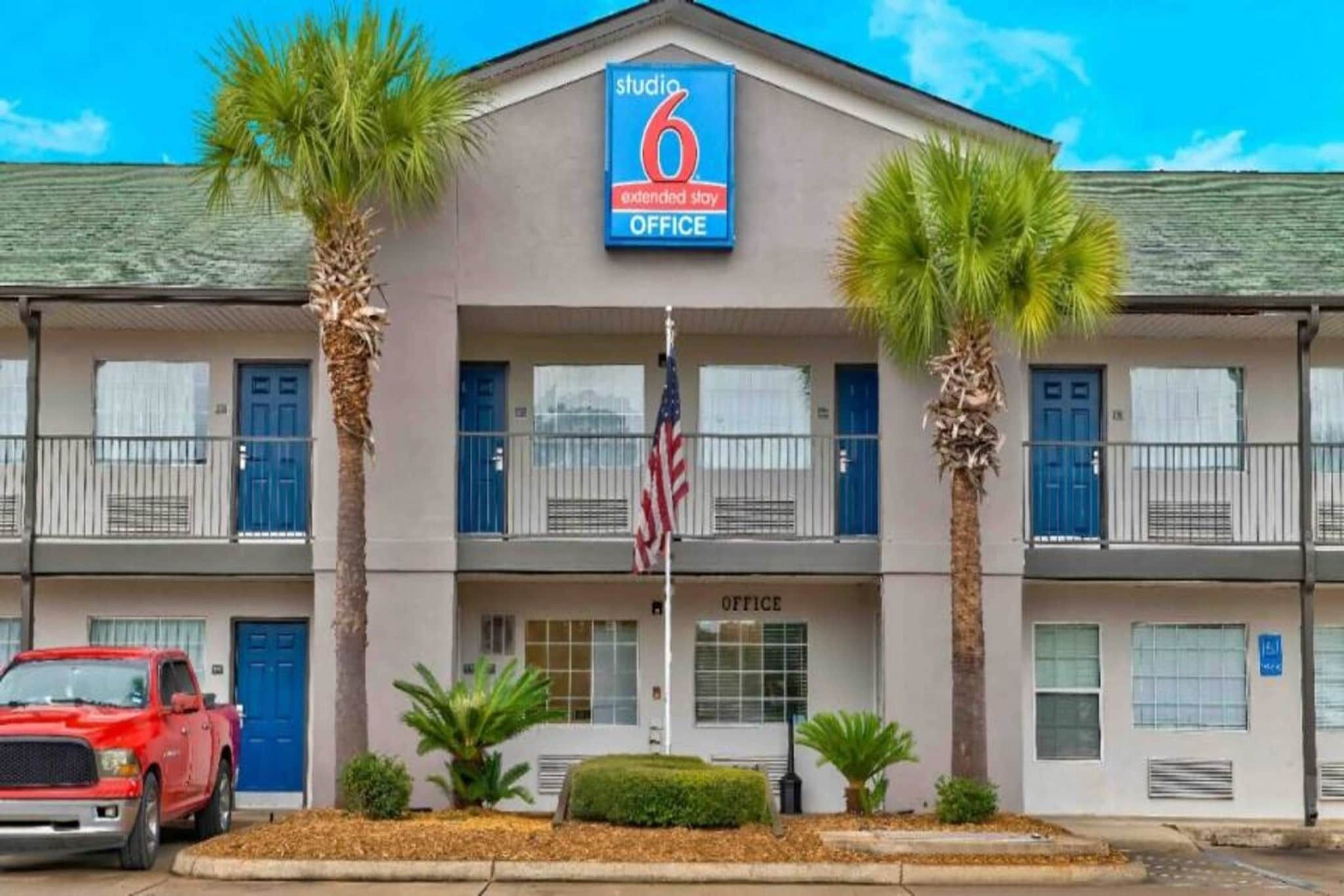 A 6 extended stay office building with a flag, palm trees, and a red truck parked in front.