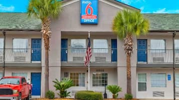 A 6 extended stay office building with a flag, palm trees, and a red truck parked in front.