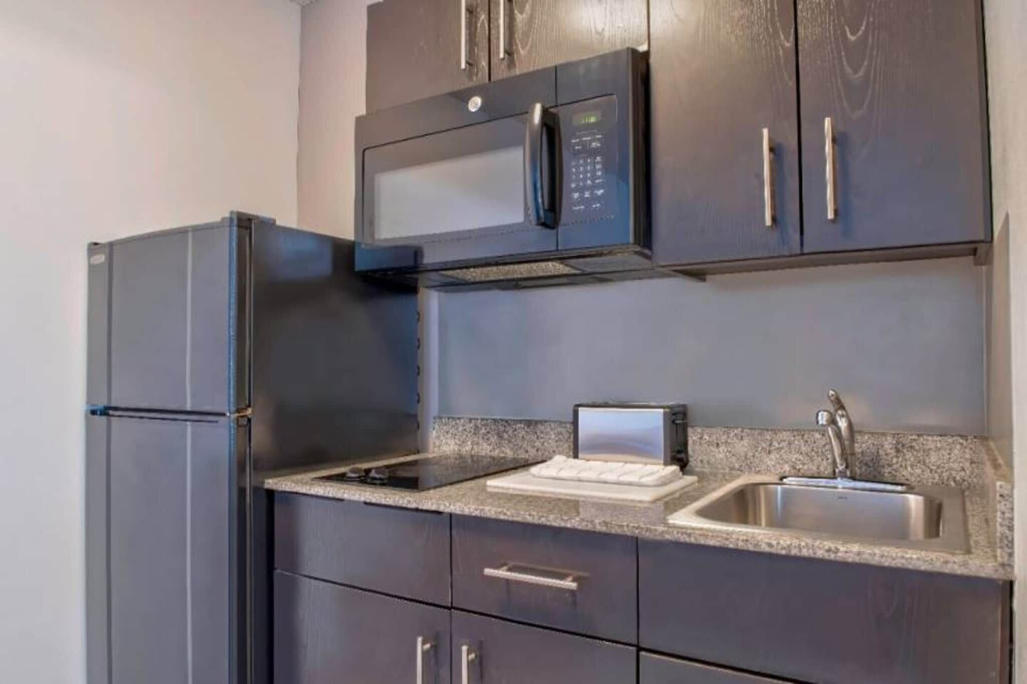 A kitchen with a refrigerator, microwave, sink, and granite countertop.
