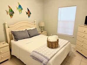 A bedroom with a bed, nightstands, a lamp, a dresser, and decorative fish wall art. - 3-bedroom pet-friendly condo in Orange Beach, sleeps 8 (Orange Beach)