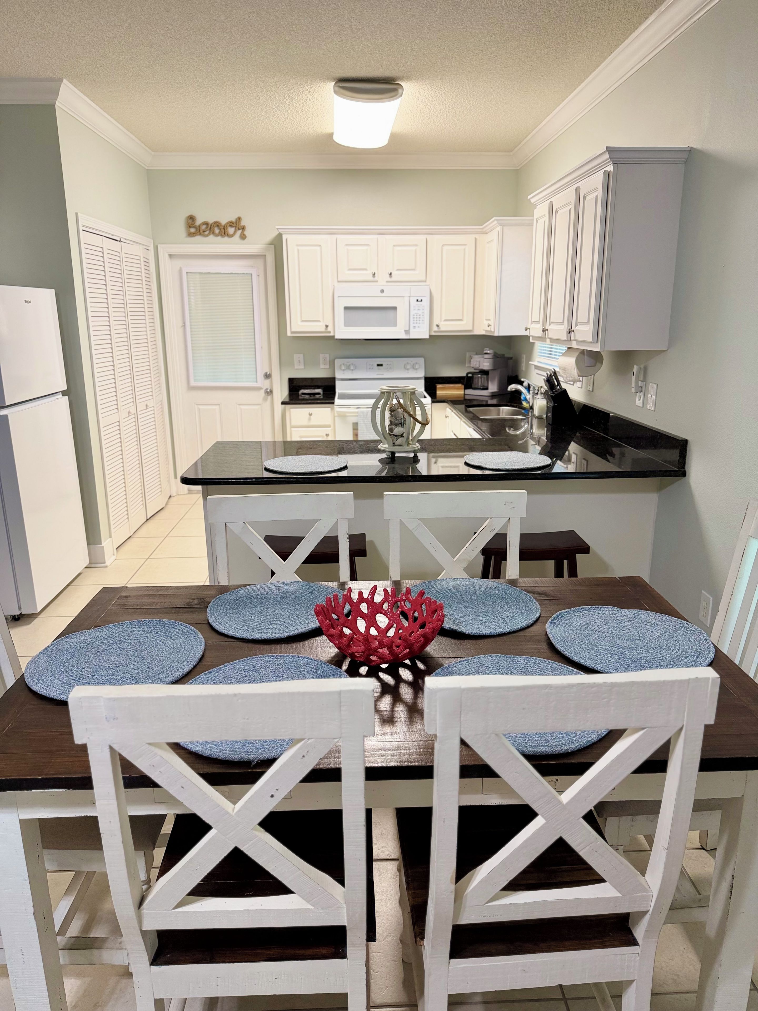 A modern kitchen with white cabinets, a central island with a microwave, and a dining area with a wooden table and white chairs.