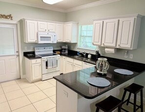 A kitchen with white cabinets, a stove, a microwave, and a coffee maker. There are two stools at the island. - 3-bedroom pet-friendly condo in Orange Beach, sleeps 8 (Orange Beach)