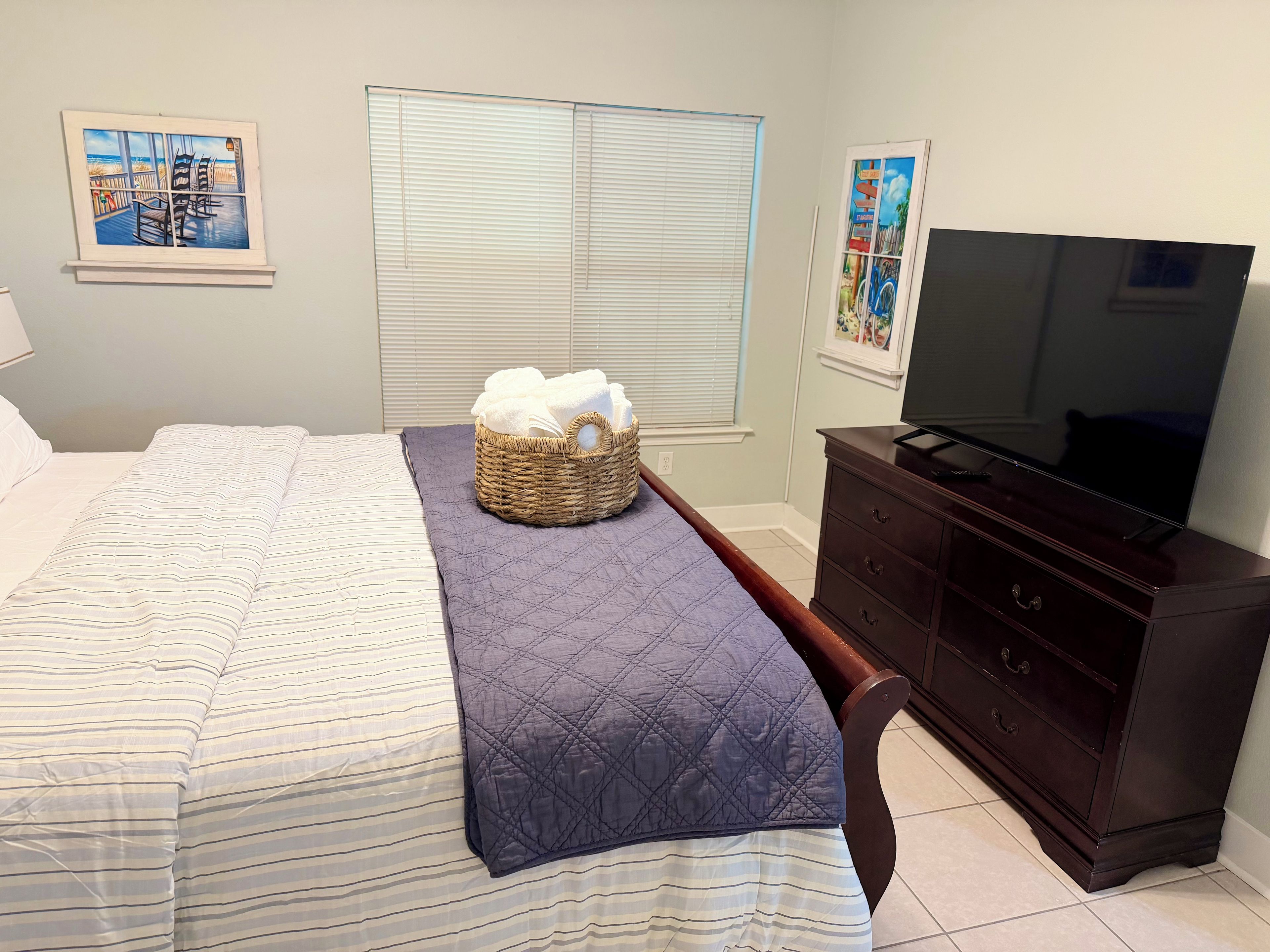 A bedroom with a bed, a television, a dresser, and a window with blinds.
