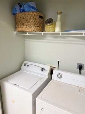 A laundry area with two white washing machines, a wicker basket, a bottle, and a shelf with a blue towel. - 3-bedroom pet-friendly condo in Orange Beach, sleeps 8 (Orange Beach)