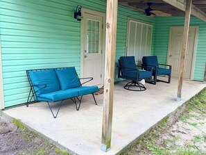 A porch with a blue sofa and two chairs, wooden posts, and a green exterior wall. - 3-bedroom pet-friendly condo in Orange Beach, sleeps 8 (Orange Beach)