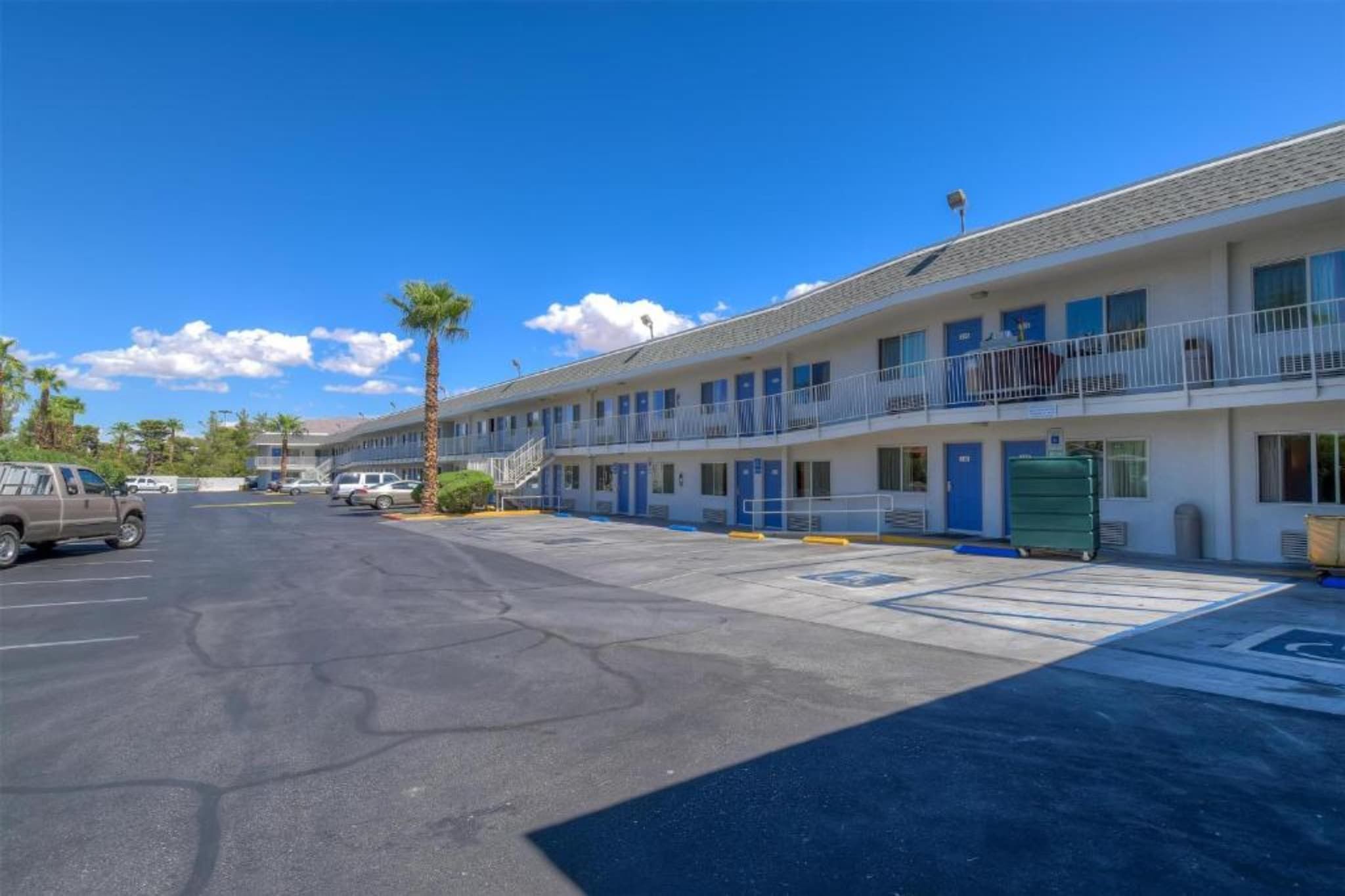 A motel with a parking lot, multiple rooms, and a clear sky.