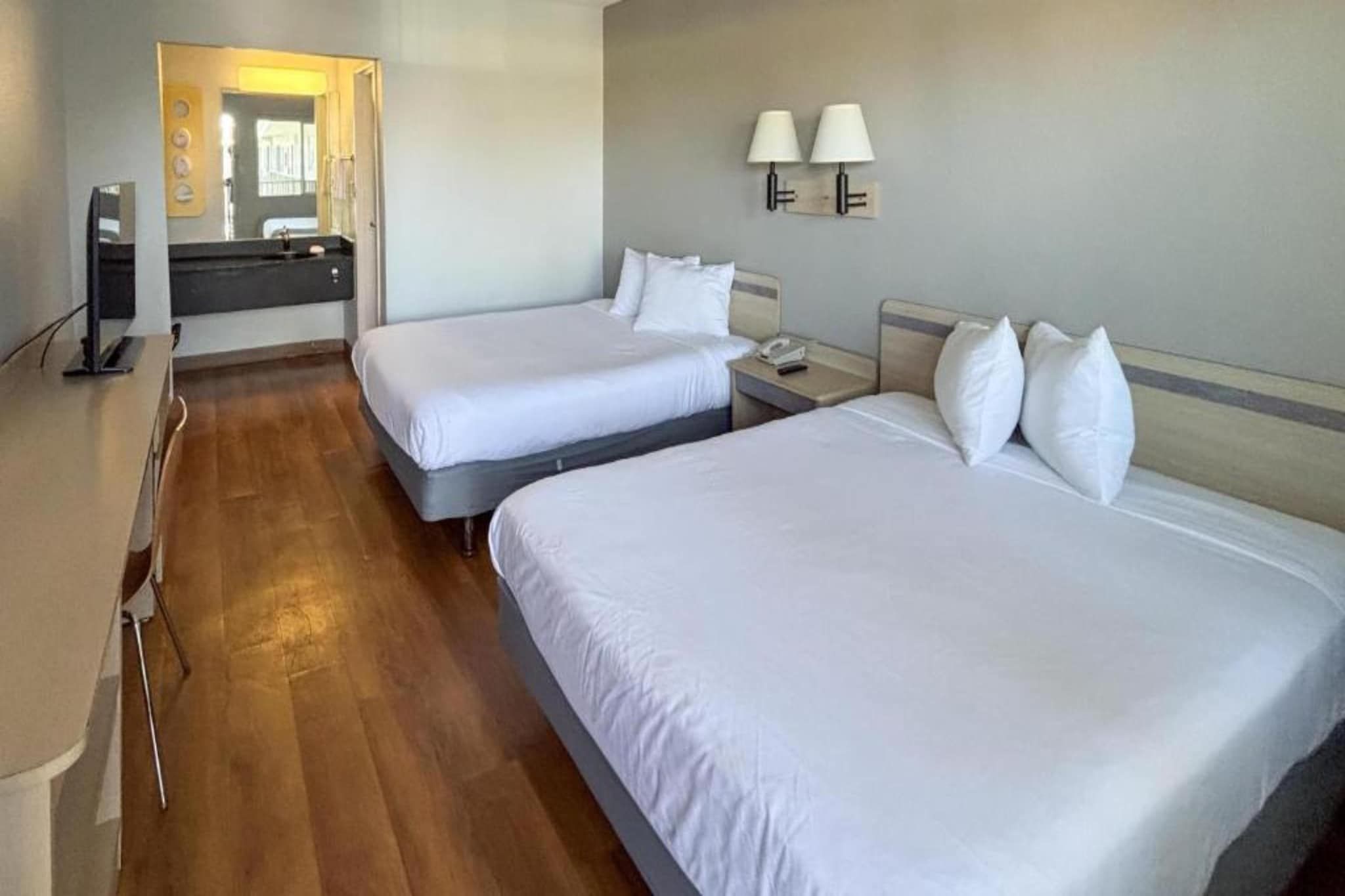 A hotel room with two beds, a desk, a mirror, and a bathroom visible through an open door.