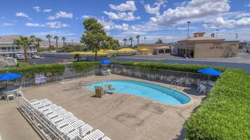 A swimming pool with lounge chairs and umbrellas, surrounded by a fence and greenery.