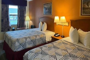 Habitación de hotel con dos camas, una mesita de noche con lámpara, teléfono y una ventana con cortinas.