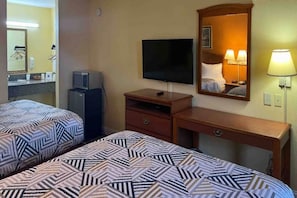 Una habitación de hotel con dos camas, televisión, escritorio, espejo y lámpara.