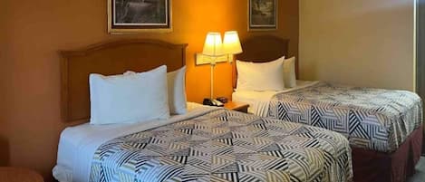 Ein Hotelzimmer mit zwei Betten, jeweils mit gemusterten Bettbezügen, einem Nachttisch mit Lampe und gerahmten Kunstwerken an den Wänden.