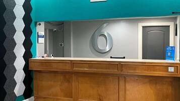 Un comptoir d’accueil avec un grand panneau indiquant le chiffre « 6 », une caméra de surveillance et un panneau d’information bleu.