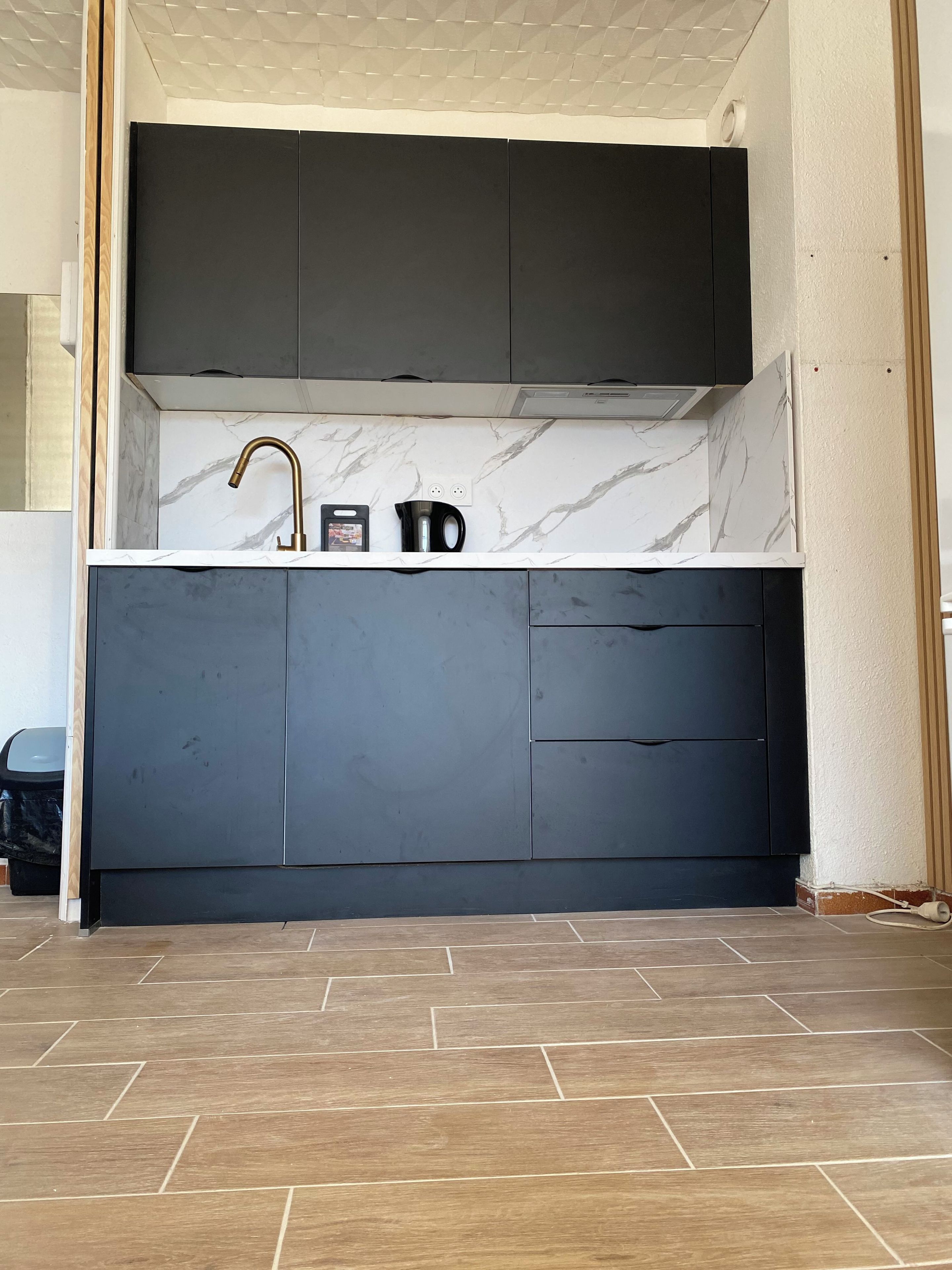 A modern kitchen with a marble backsplash, dark cabinets, and a herringbone-patterned floor.