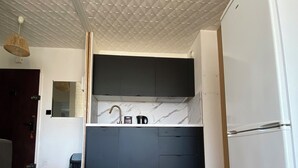 Een moderne keuken met een witte koelkast, donkere kastjes en een marmeren aanrechtblad.