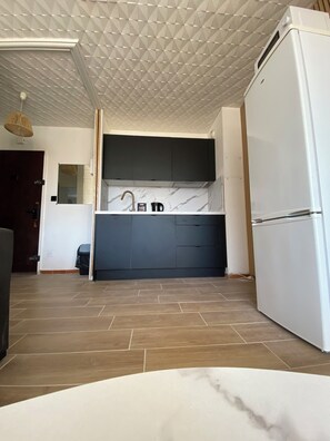 A modern kitchen with a white refrigerator, dark cabinets, and a marble countertop. - Panoramic Sea View – Cozy Renovated Apartment (Hérault)