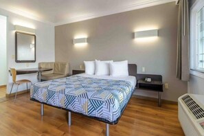 Hotellihuone, jossa on sänky, työpöytä, tuoli ja lämmitin.