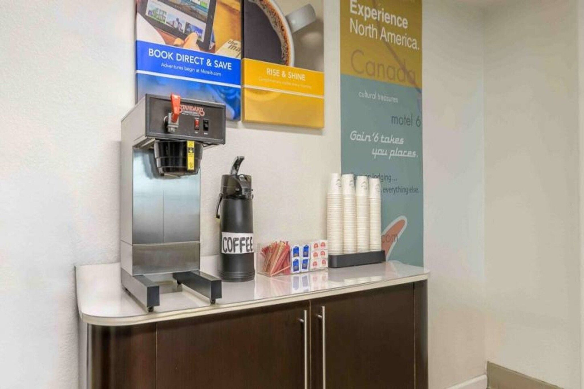 Una estación de café con una máquina de café, tazas y un cartel que promociona viajes por Norteamérica.