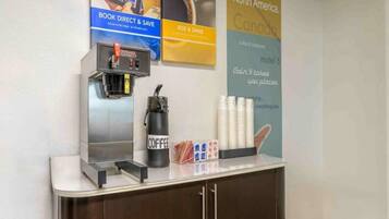 Una estación de café con una máquina de café, tazas y un cartel que promociona viajes por Norteamérica.