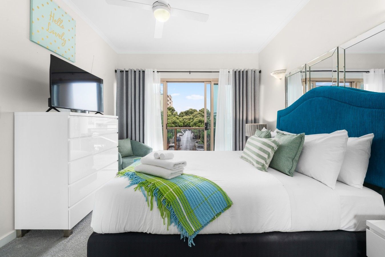 Une chambre moderne avec un grand lit, une commode, un téléviseur et un balcon agrémenté de rideaux.