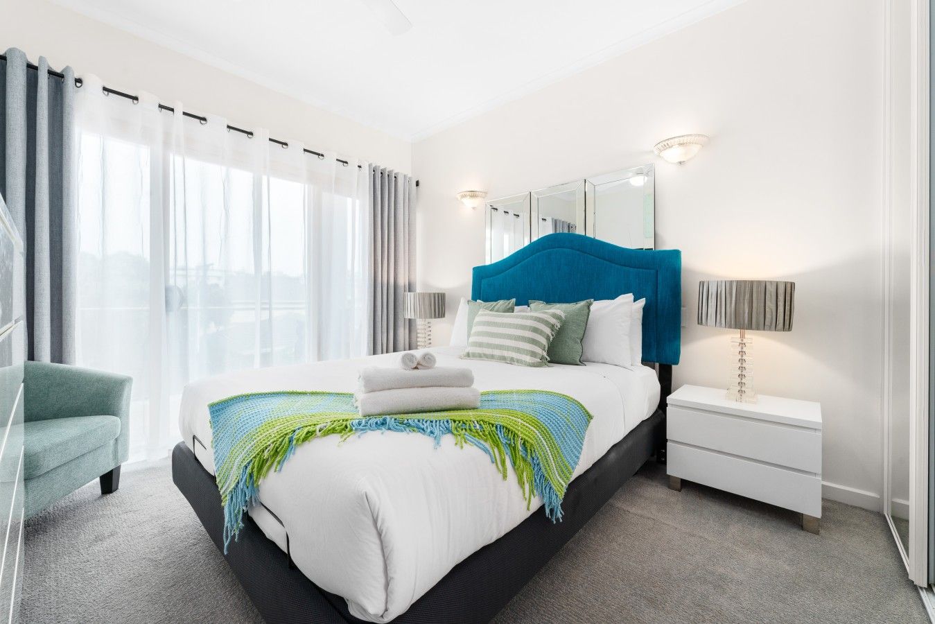 A modern hotel room with a large bed, a bedside table, a chair, and a window with curtains.
