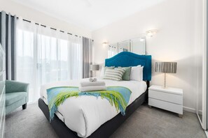 Ein modernes Hotelzimmer mit einem großen Bett, einem Nachttisch, einem Sessel und einem Fenster mit Vorhängen.