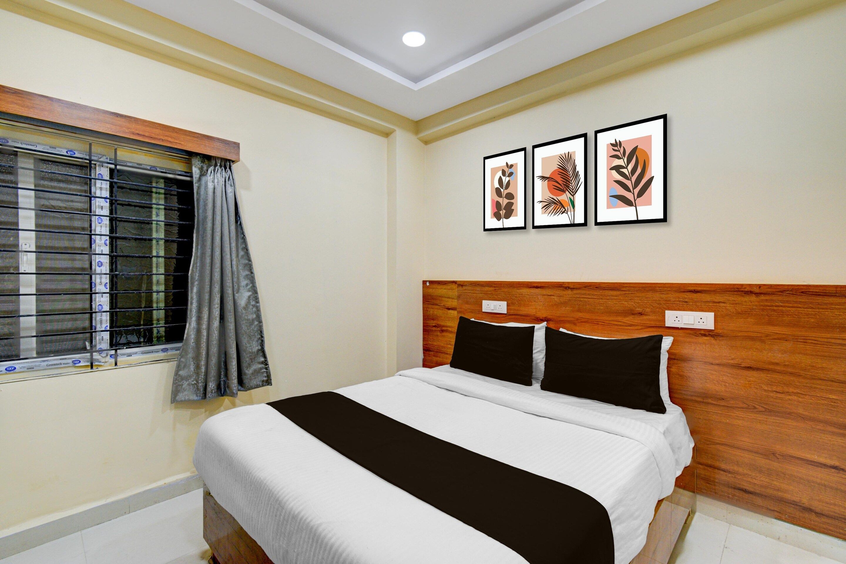 A bedroom with a bed, a window with blinds, and three framed pictures on the wall.