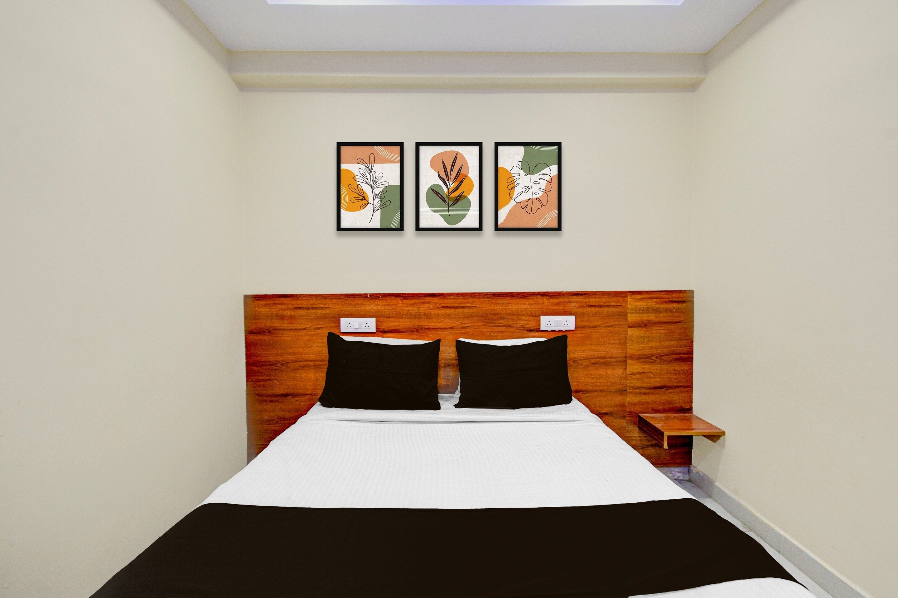 A hotel room with a bed, a wooden headboard, a nightstand, and three framed artworks on the wall.