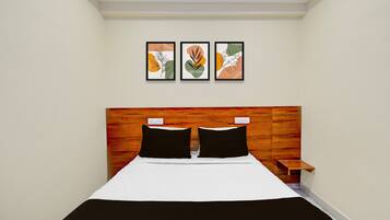 A hotel room with a bed, a wooden headboard, a nightstand, and three framed artworks on the wall.