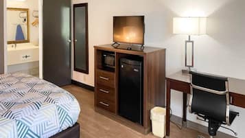 Quarto de hotel com cama, escrivaninha, cadeira, televisão, luminária e armário.