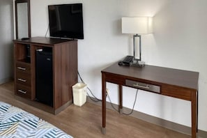Ett hotellrum med ett skrivbord i trä, en tv, en lampa och en papperskorg.