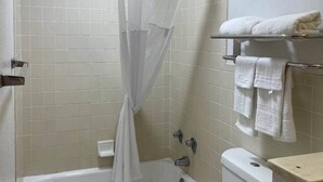 A bathroom with a bathtub, a toilet, and a shower curtain. - 1 King Bed|Smoking|Opelika, AL (Opelika AL)