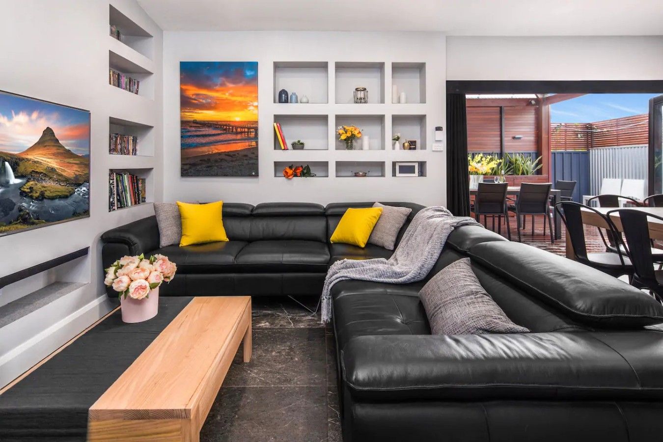 Ein modernes Wohnzimmer mit einer schwarzen Ledersofa, einem Holztisch und einem großen Gemälde von einem Sonnenuntergang.