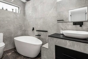 Een moderne badkamer met een vrijstaand bad, een witte wastafel en een grote spiegel.