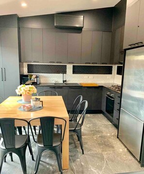 Een moderne keuken met donkere kastjes, een houten eettafel en een roestvrijstalen koelkast.
