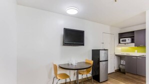 Een compacte keuken met een koelkast, magnetron en een eethoek met twee stoelen en een tafel.