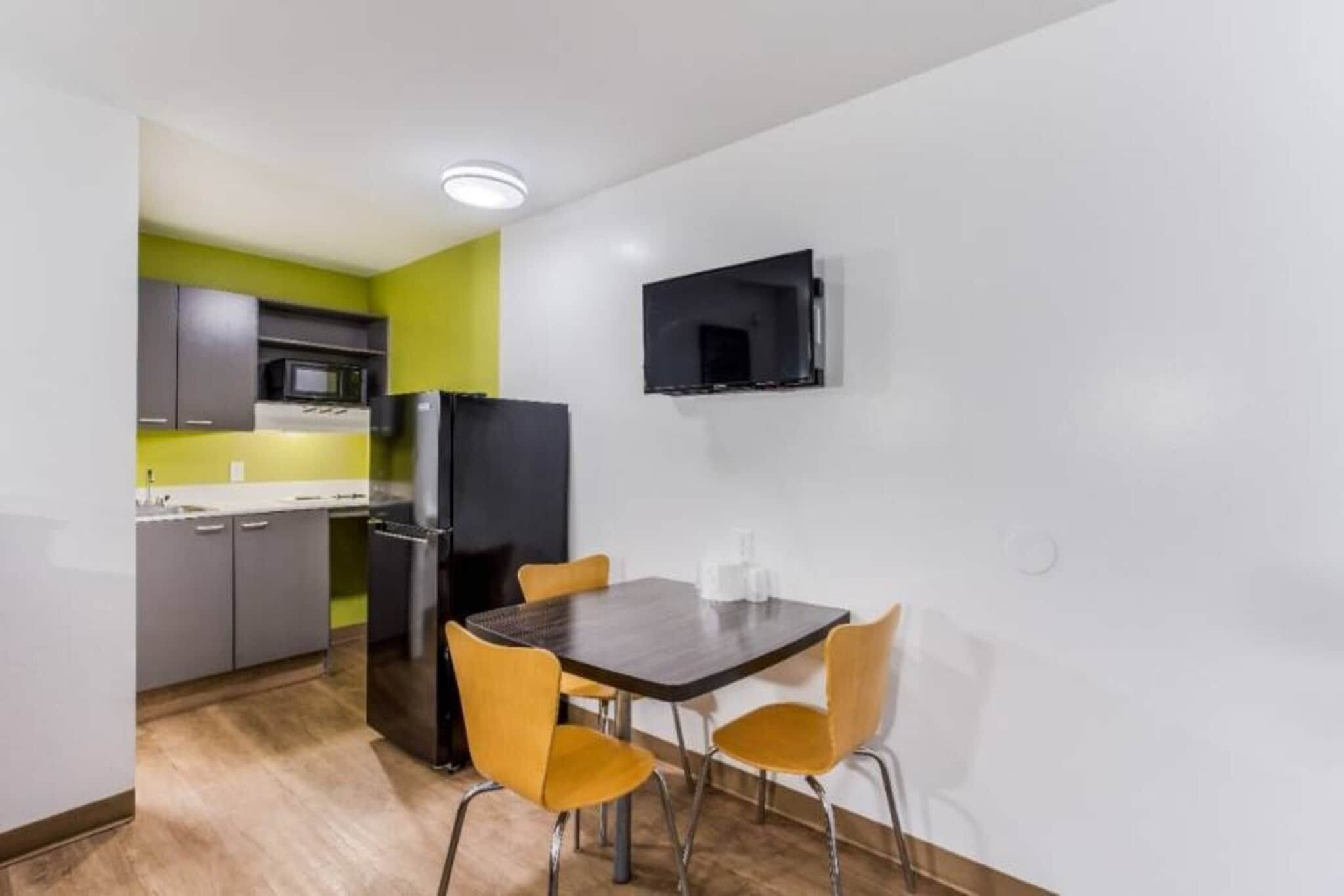 A compact kitchen with a dining area, including a table and chairs, a refrigerator, and a microwave.