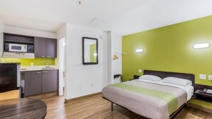 Een kleine hotelkamer met een bed, een bureau en een kitchenette.