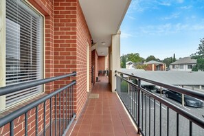 Ein Balkon mit Metallgeländer, einer Ziegelwand und Blick auf eine Straße mit geparkten Autos.