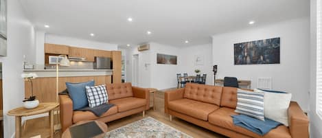 Una sala de estar moderna con dos sofás, una mesa de centro y un comedor con mesa y sillas.