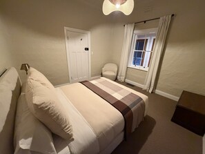 Ein Schlafzimmer mit einem Bett, einem Sessel, einem Fenster mit Vorhängen und einer Tür.
