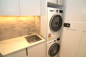 Een kleine wasruimte met een ingebouwde wasmachine en droger, een roestvrijstalen spoelbak en een betegelde achterwand.