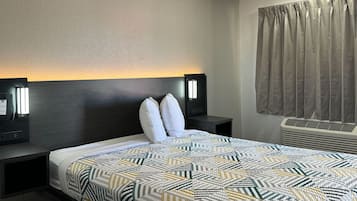 A hotel room with a bed, two bedside tables with lamps, a window with curtains, and an air conditioning unit.