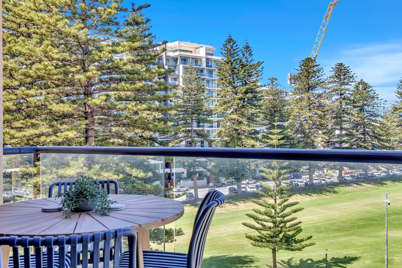 Un balcon avec une table et des chaises, donnant sur une pelouse et un parking rempli de voitures.