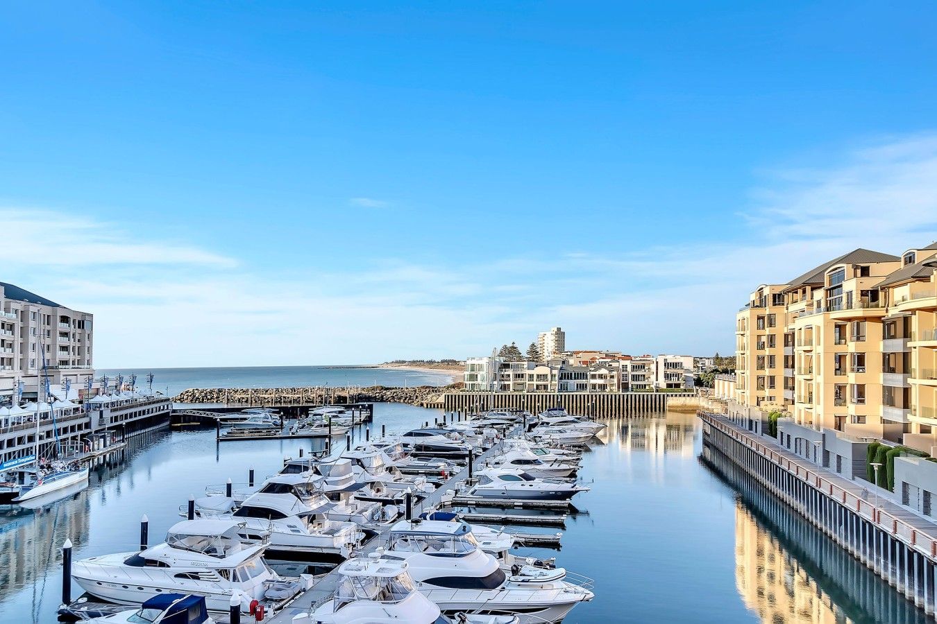 A marina with boats docked, a waterfront promenade, and buildings along the shore.