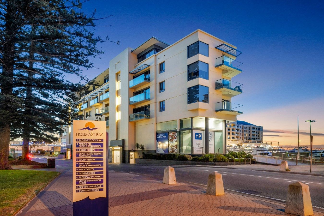 A multi-story hotel with a modern design, featuring balconies, large windows, and a signboard with directional information.