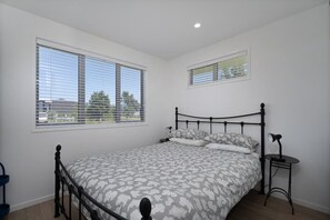 Ein Schlafzimmer mit einem Bett, zwei Fenstern, einem Nachttisch und einer Lampe.
