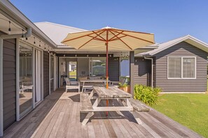 Ein überdachter Außenbereich mit Picknicktisch und Sonnenschirm, direkt neben einem Haus mit Schiebeglastür.
