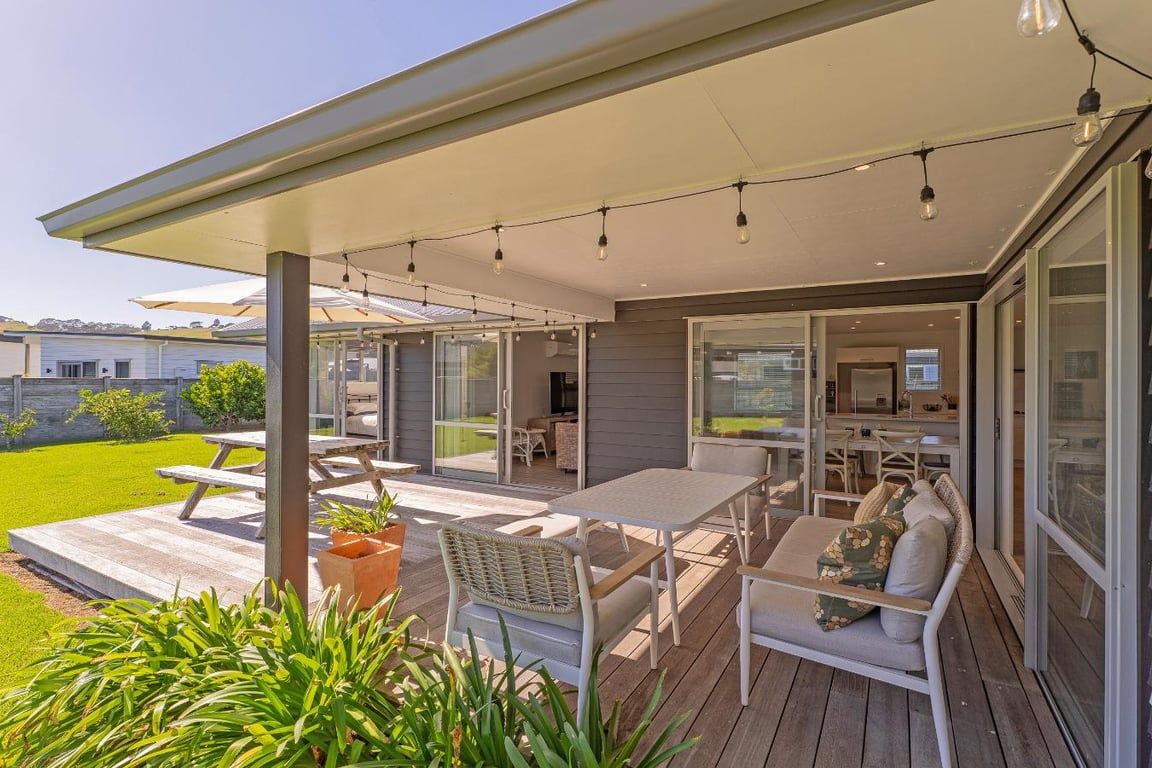 Een terras buiten met een tafel en stoelen, een bank, en een pergola met lichtslingers.