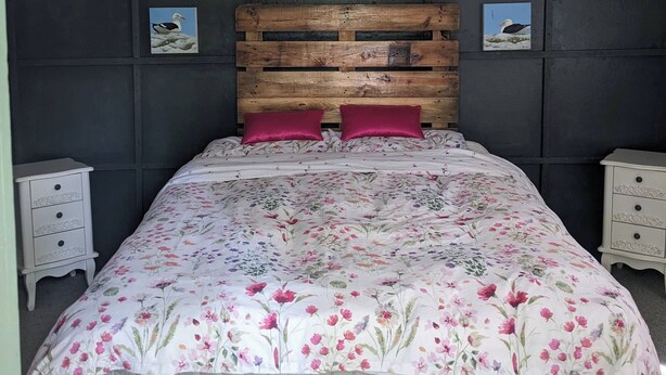 A bed with a floral bedspread, a wooden headboard, and two nightstands with drawers.